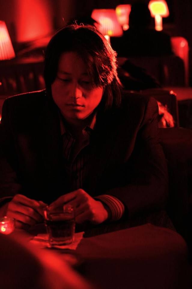 a person sitting at a table with a glass in front of them and a red light behind them