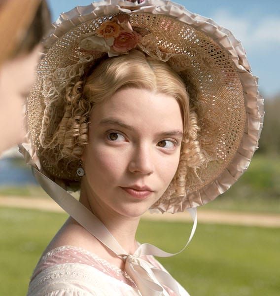 a woman wearing a large hat with flowers on it's head and another woman looking at her