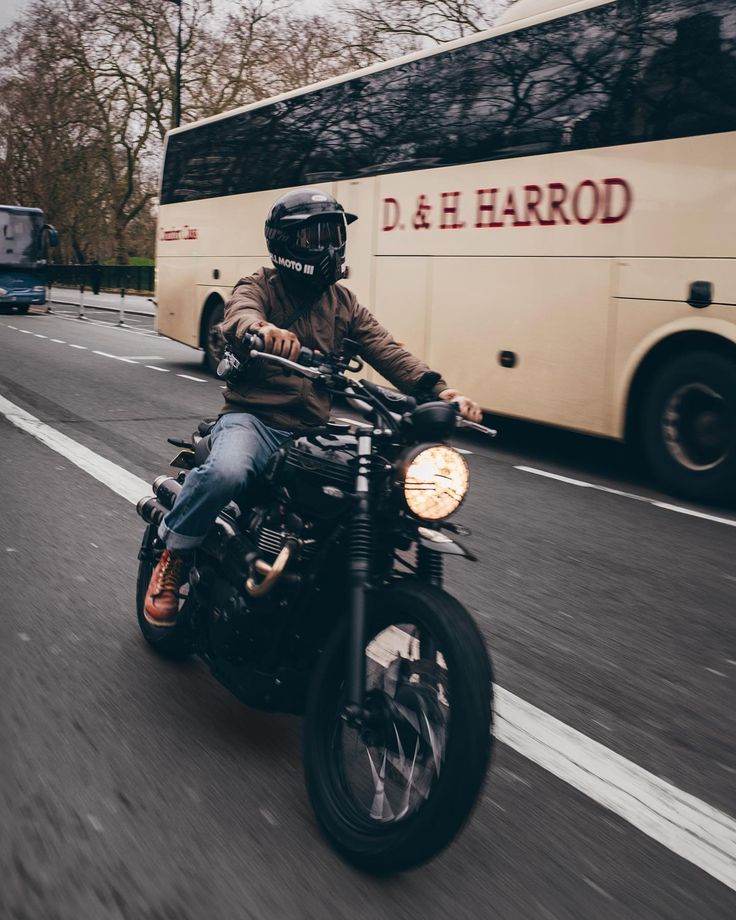 a man riding on the back of a motorcycle down a street next to a bus