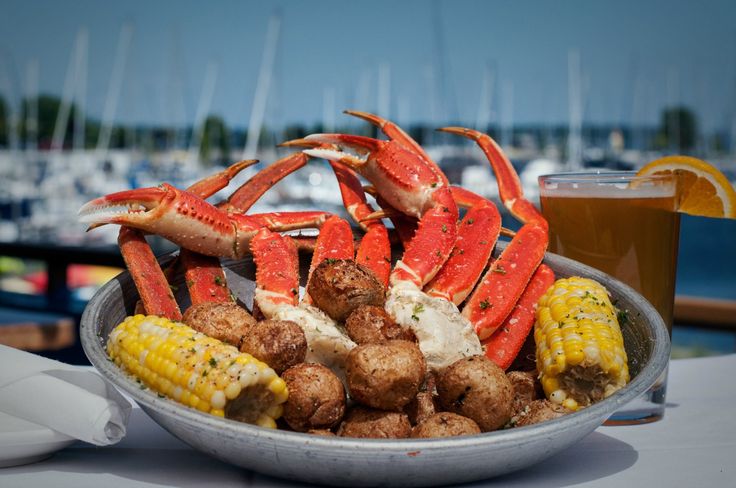 crab legs, corn on the cob and potatoes in a bowl with a glass of beer