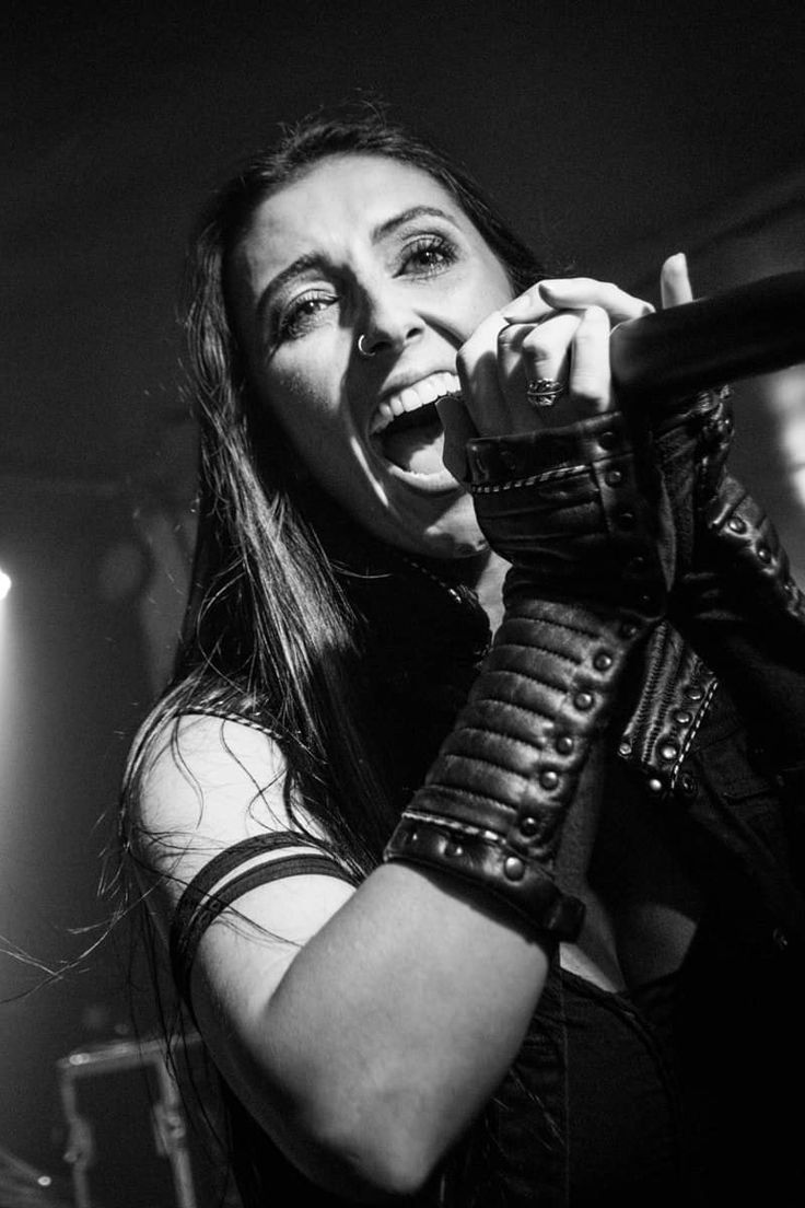 a woman singing into a microphone while holding her hands up in the air and wearing leather gloves