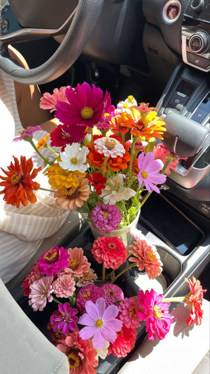 a bunch of flowers in a vase sitting on the dash board of a car,