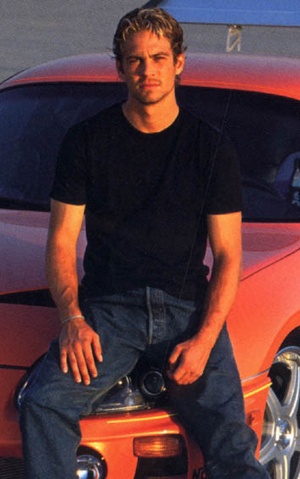 a man sitting on the hood of an orange sports car with his feet propped up
