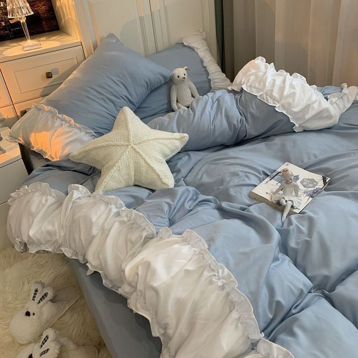 a bed with blue sheets and white ruffles is shown in this image, there are two stuffed animals on the side of the bed