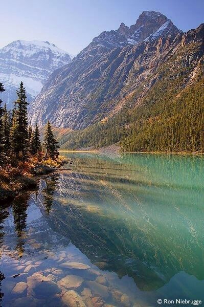 the mountains are covered in snow and green water, with trees on both sides of the lake