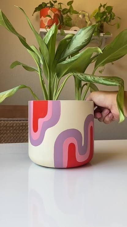 a hand is holding a potted plant on a table