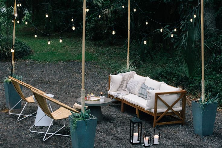 an outdoor seating area with lights strung from the ceiling and potted plants on the ground