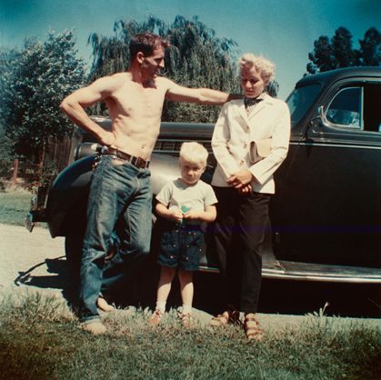 an older man and two young boys standing in front of a car