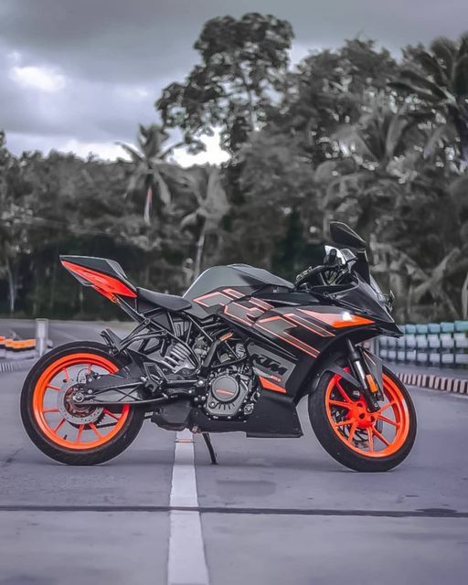 a black and orange motorcycle parked in a parking lot next to palm trees on a cloudy day