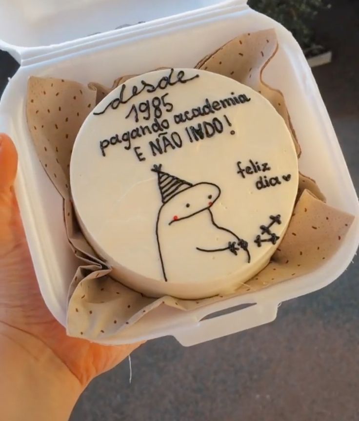 a person holding up a cake in a container with writing on the side and an image of a dog wearing a party hat