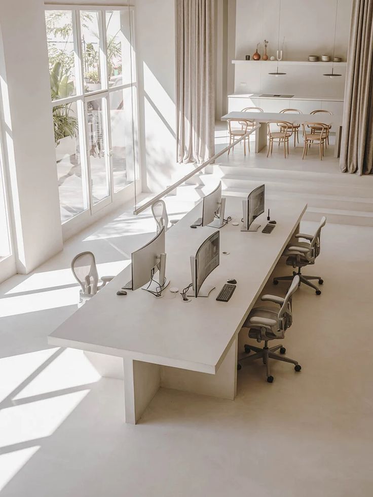 an office with multiple computer screens and desks in front of large windows that look out onto the outdoors