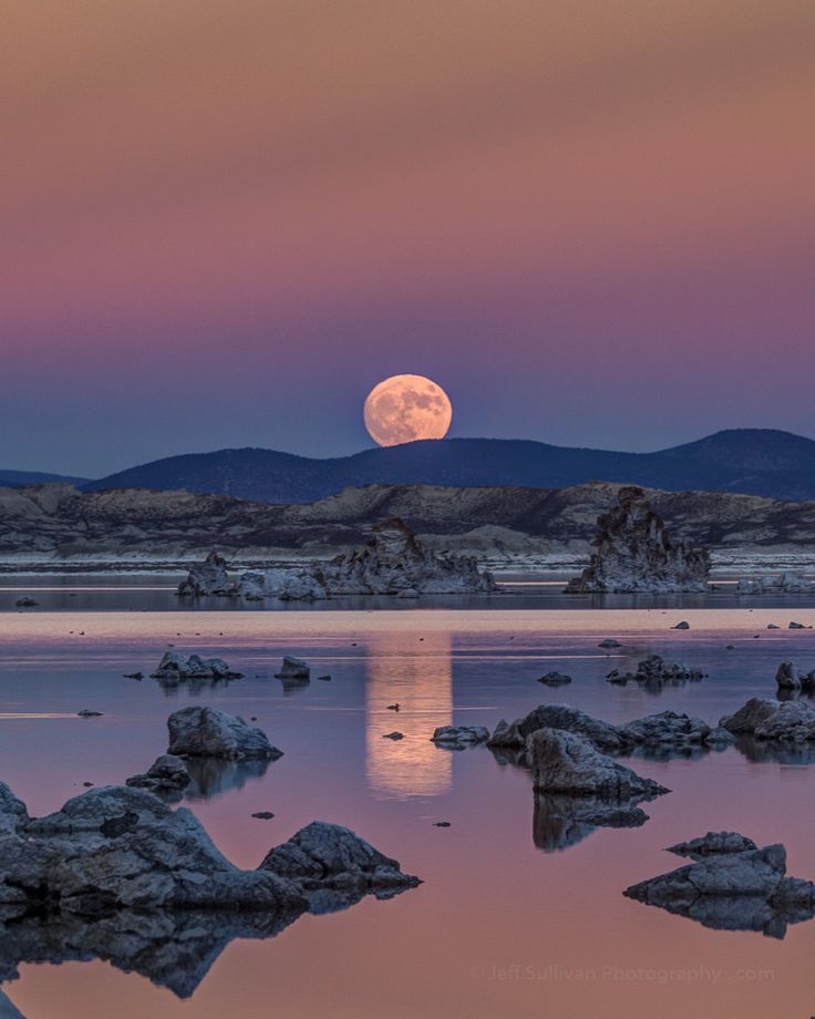 the moon is setting over some rocks and water