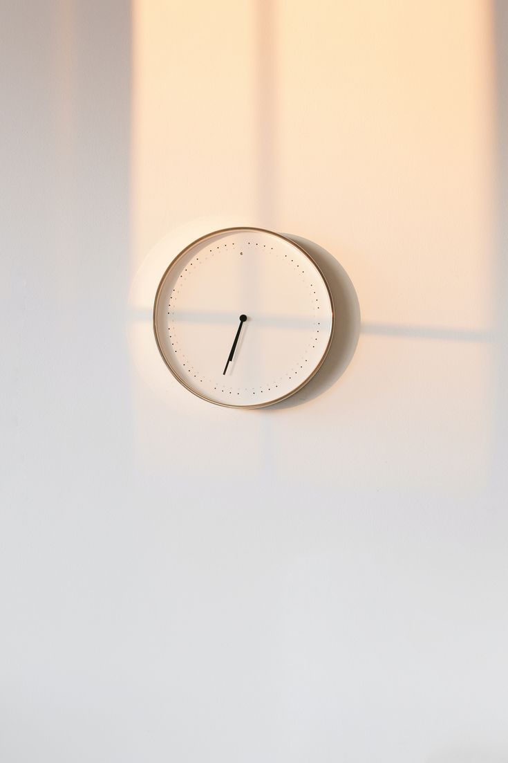 a white clock on the wall with shadow from it's face and light coming through the window