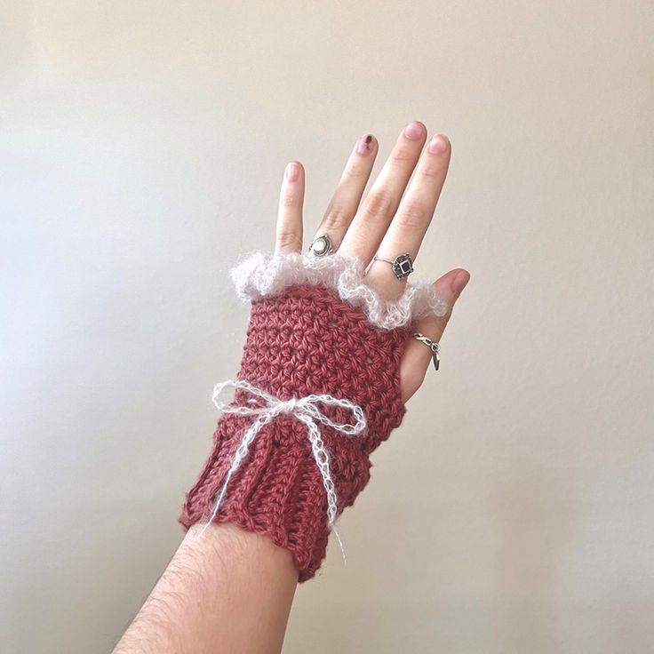 a woman's hand wearing a crocheted red mitt with white lace