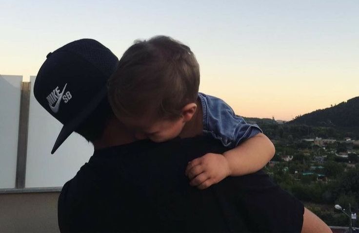 a man holding a baby in his arms on top of a roof with mountains in the background