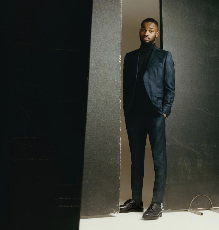 a man standing in front of a mirror wearing a black suit and turtle neck sweater