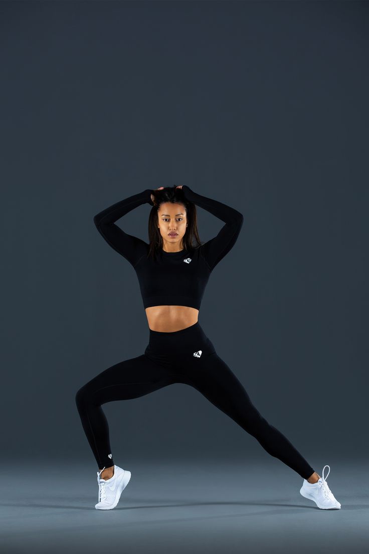 a woman in black sports bra top and leggings with her hands behind her head