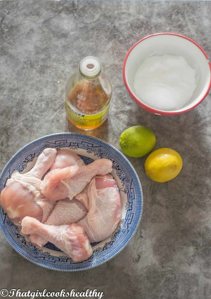 raw chicken in a blue bowl next to lemons and water
