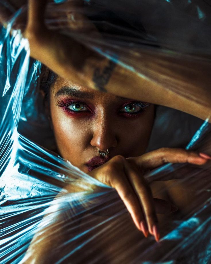 a woman with blue eyes and piercings wrapped up in plastic foil looking at the camera