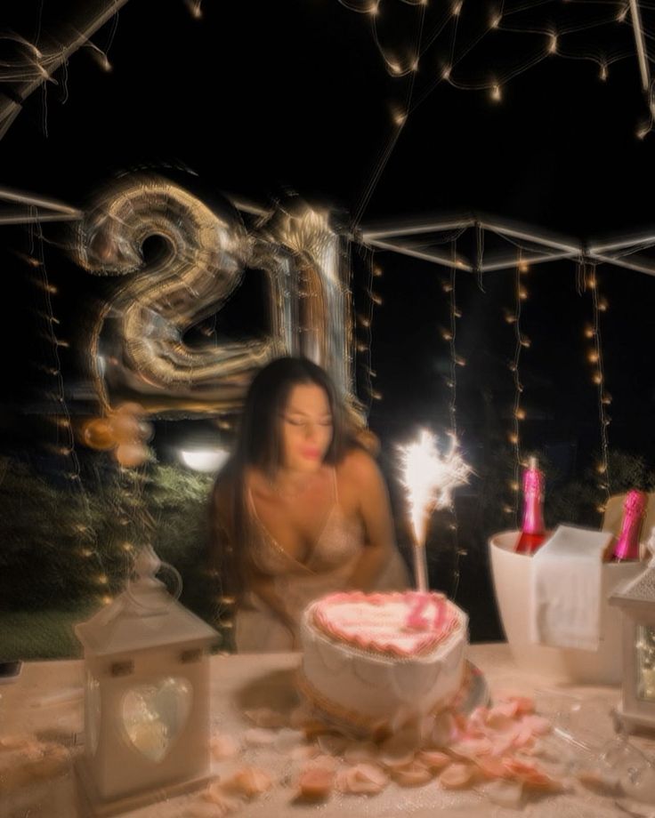 a woman sitting at a table in front of a cake with lit candles on it