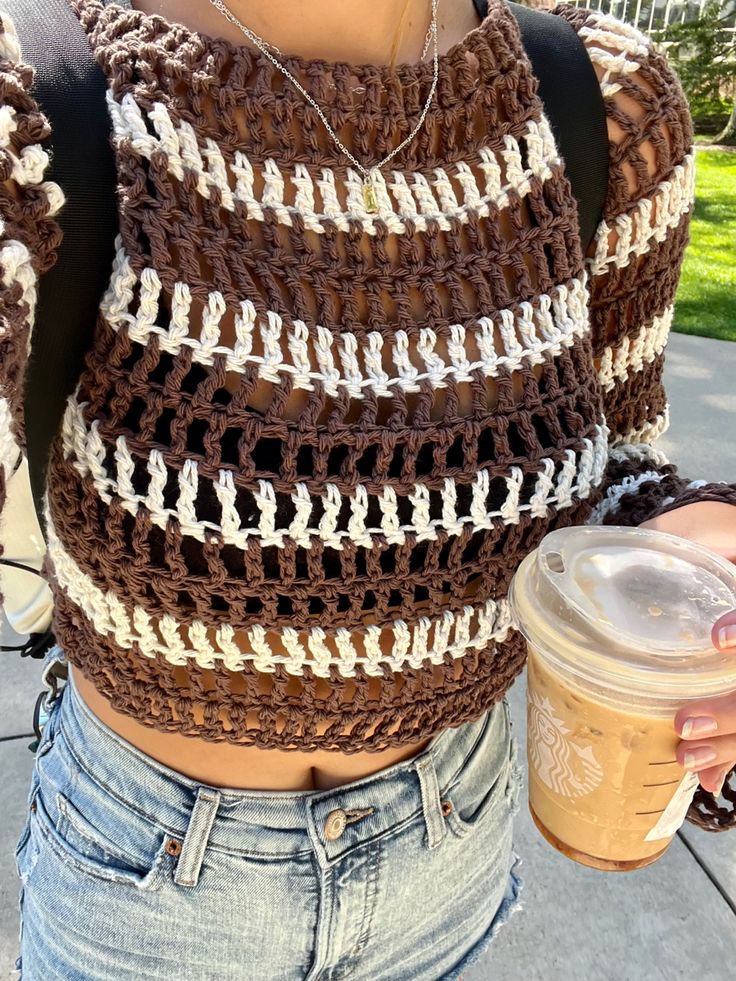 a close up of a person holding a drink and wearing a crocheted sweater