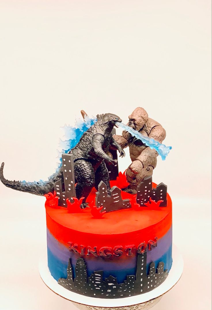 two toy dinosaurs on top of a red and blue cake