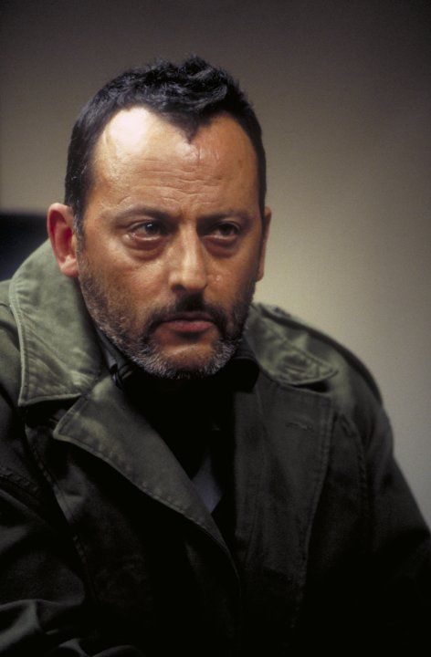 a man with a beard wearing a black shirt and green jacket looking at the camera