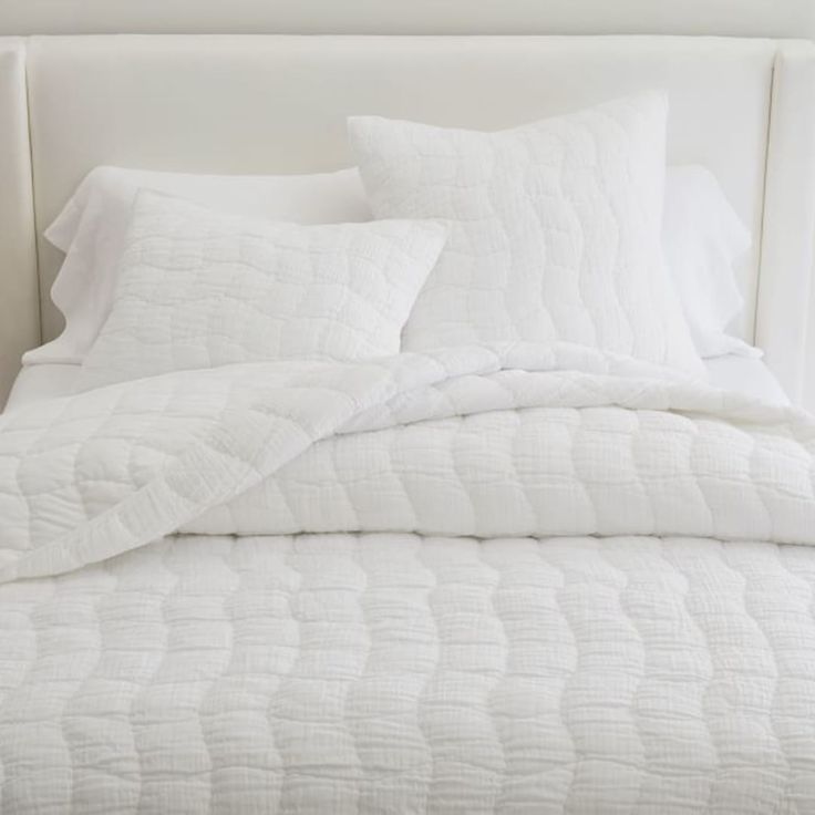 a bed with white sheets and pillows on it