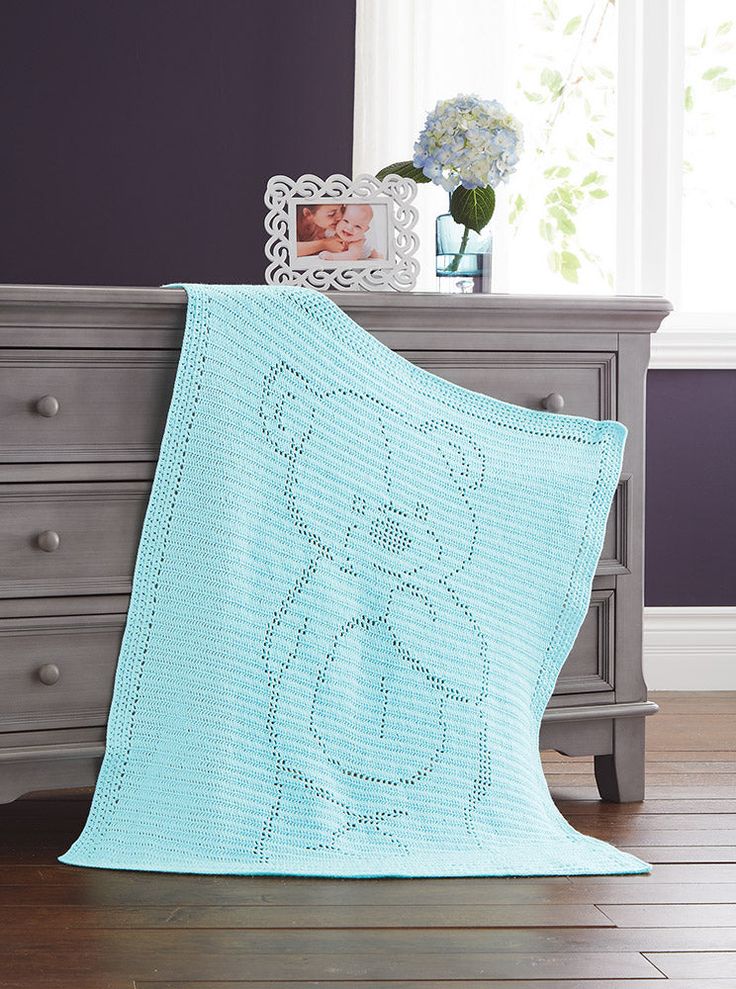 a blue crocheted teddy bear blanket sitting on top of a dresser next to a window