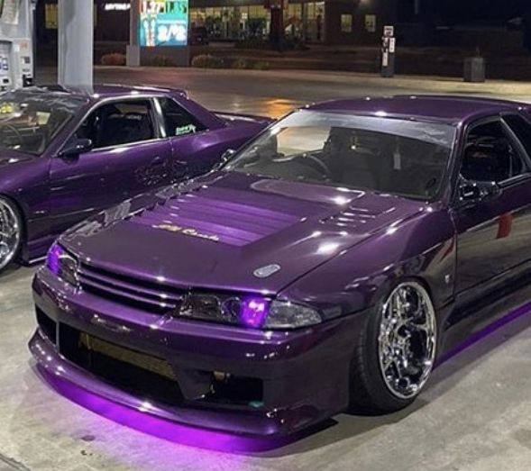 two purple cars parked next to each other in a parking lot with lights on them