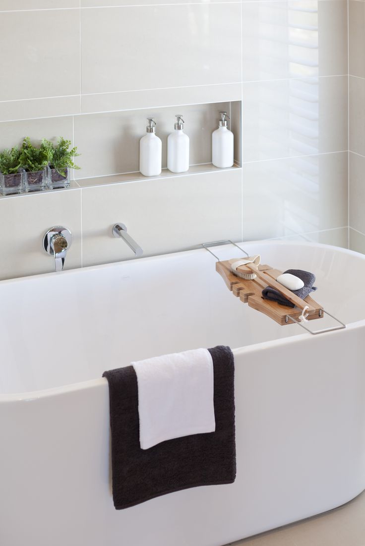 a white bath tub sitting under a window next to a shelf with soap and toothbrushes