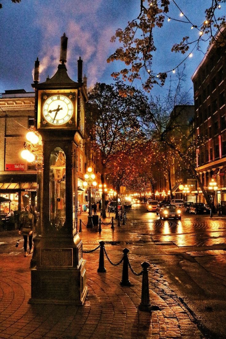 a clock tower sitting in the middle of a street at night time with people walking around