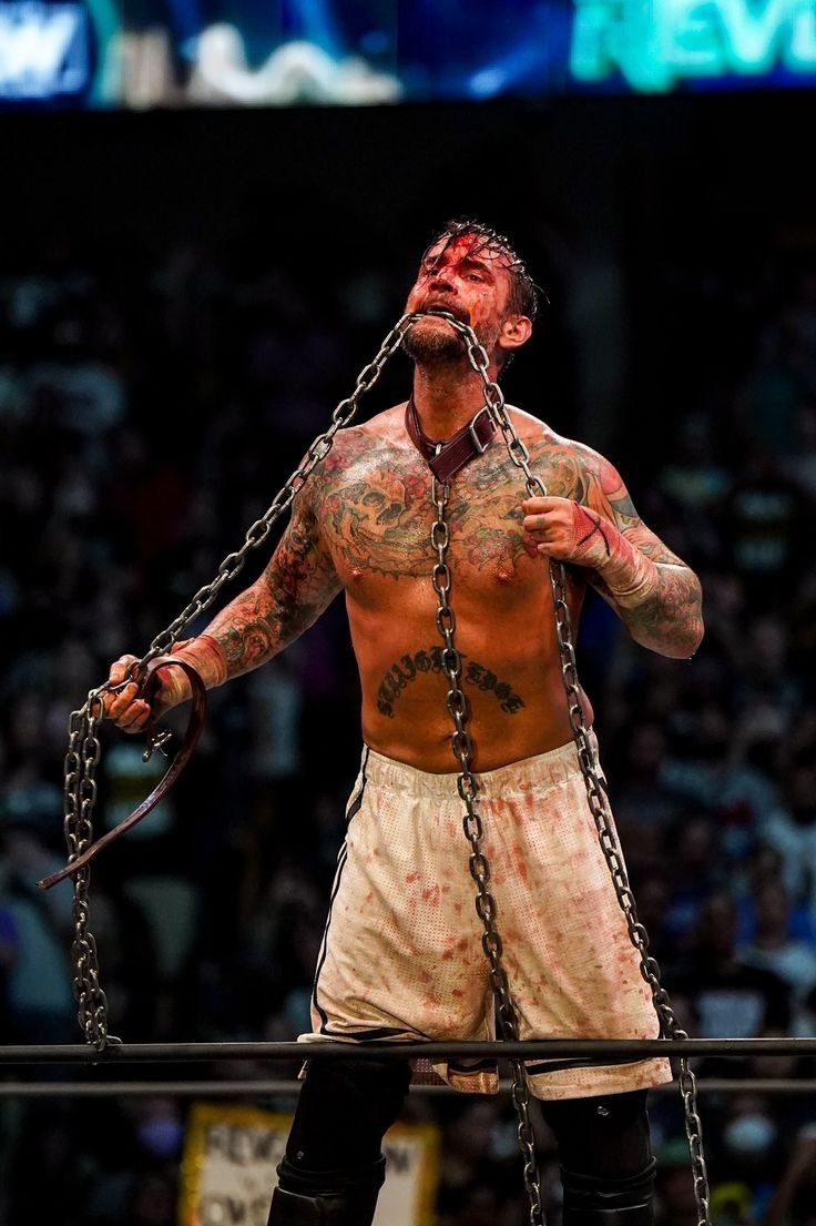a man with tattoos and chains around his neck standing in front of a crowd at a wrestling match