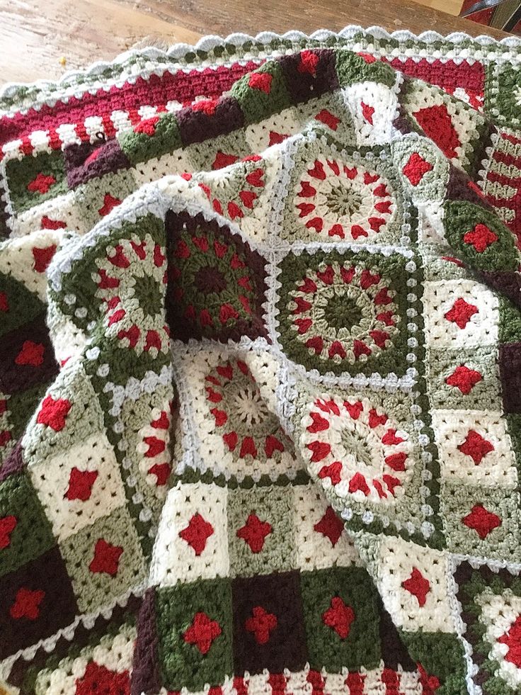 a crocheted blanket with red, green and white designs on it sitting on a wooden floor