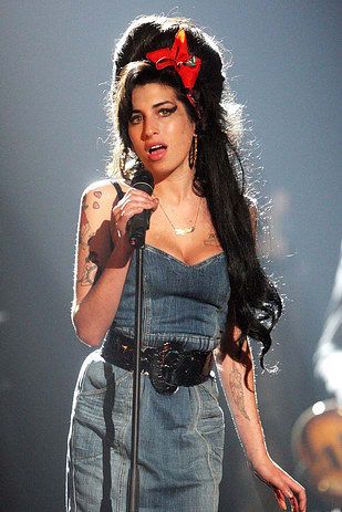 a woman with long hair holding a microphone in front of her face and wearing a denim dress