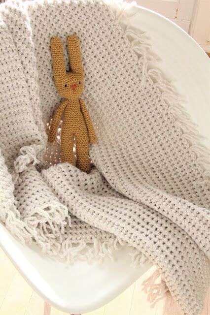 a small stuffed animal sitting on top of a white chair under a knitted blanket