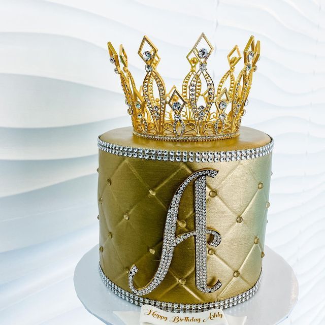 a gold and white cake with a tiara on top that is decorated with diamonds