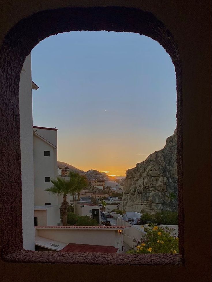 the sun is setting over some buildings and mountains as seen through an arch in a building