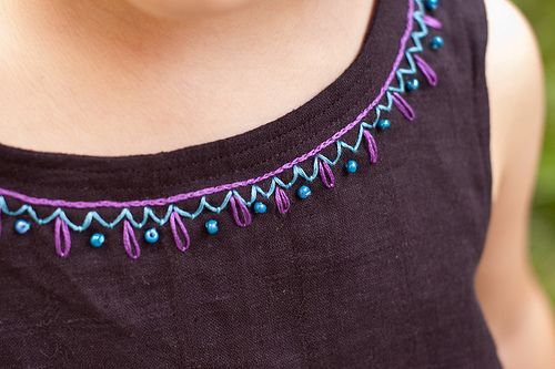 a woman wearing a black top with purple and blue beads on it's neck