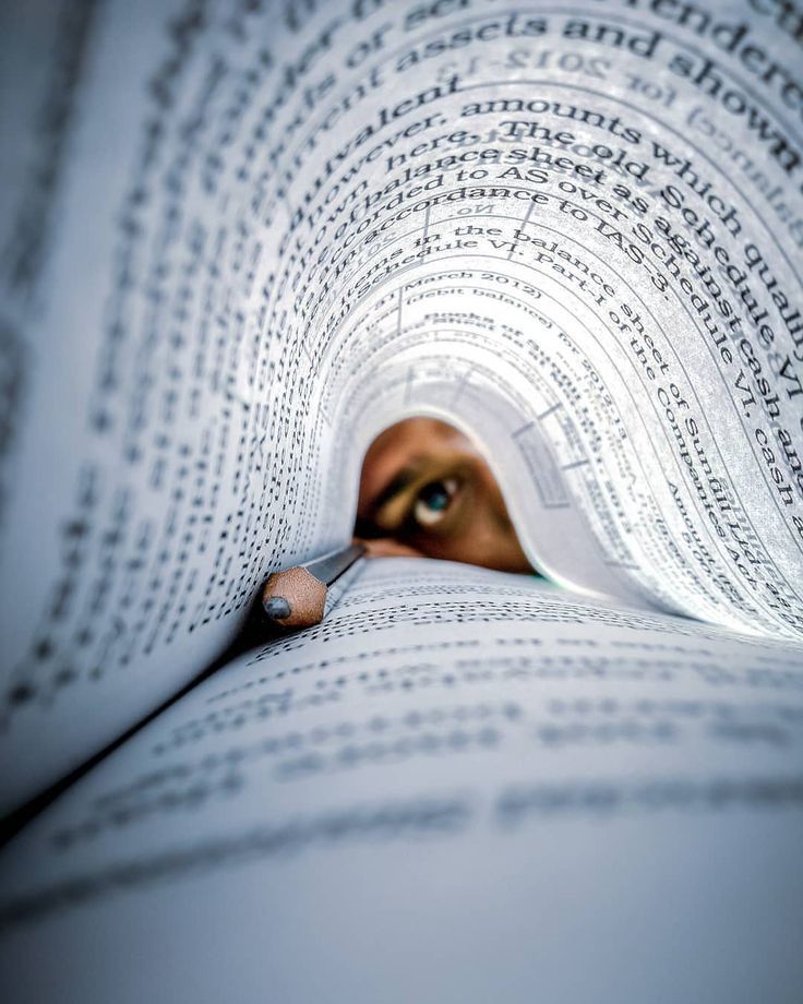 a close up of a person's eye peeking out from the pages of a book