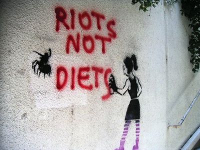 graffiti on the side of a building that says riots not diets with an image of a woman holding a knife