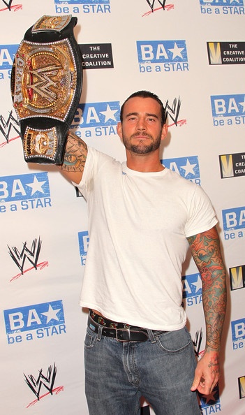 a man holding up a wrestling belt in front of a wall