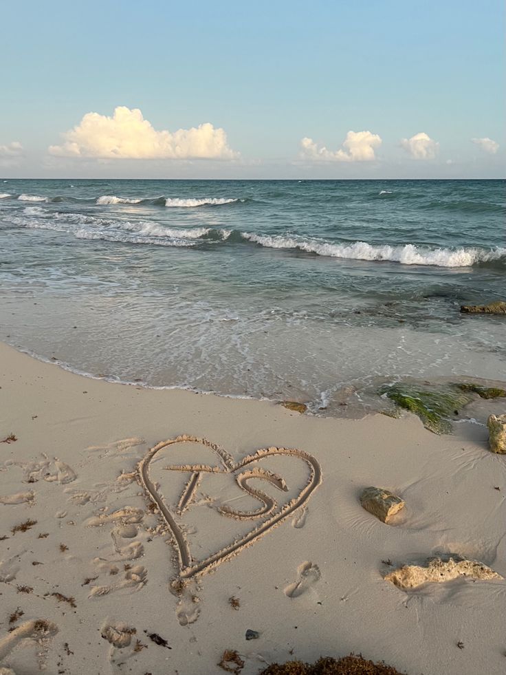 a heart drawn in the sand on a beach next to the ocean with waves coming in