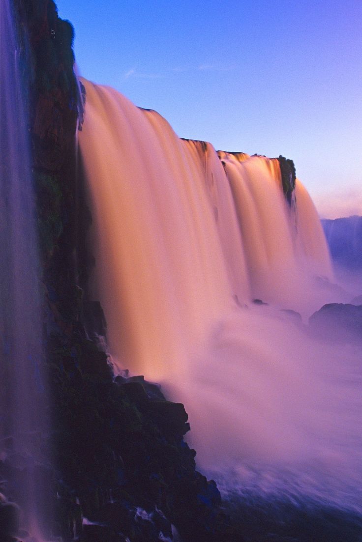 a waterfall with water pouring out of it's sides into the air at sunset