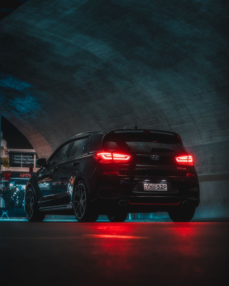 a black car parked under a tunnel with red lights on it's taillights