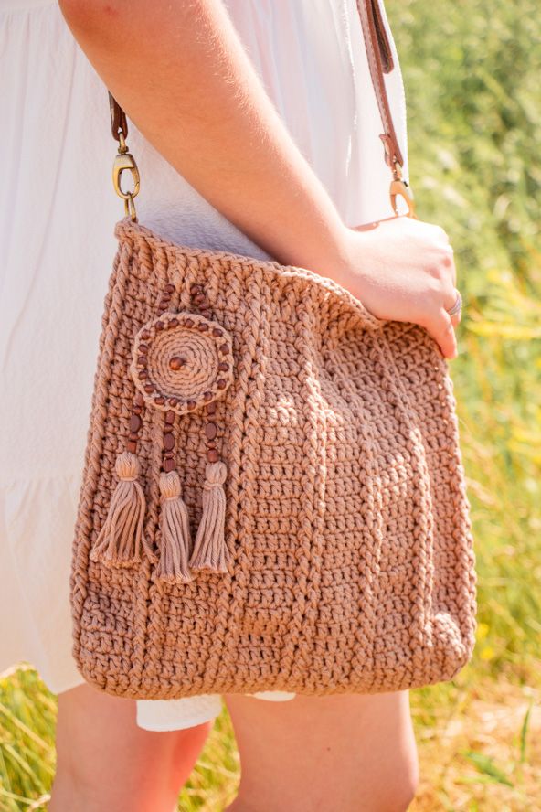 a woman holding a brown crocheted bag with tassels on the handles