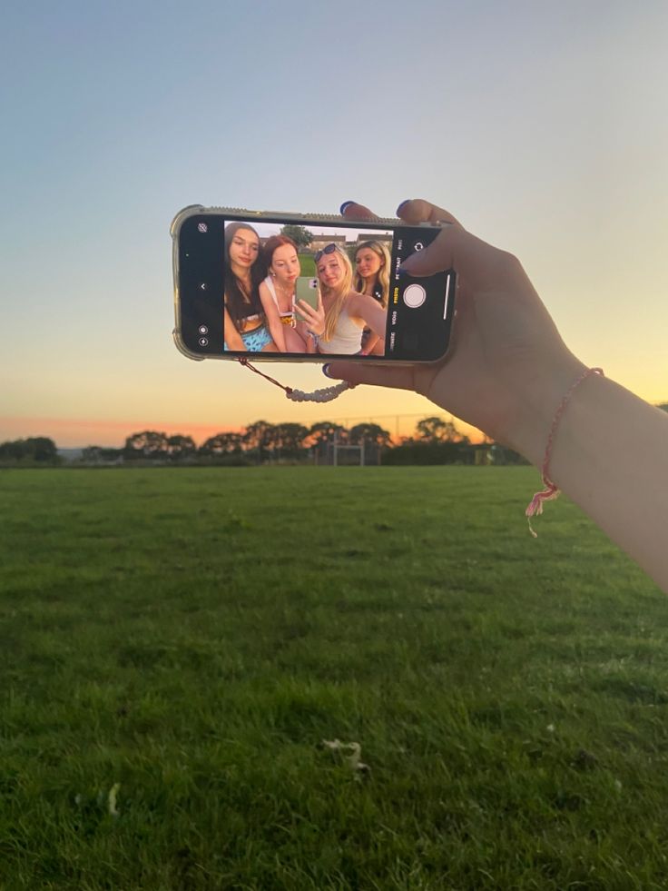 a person holding up a cell phone to take a photo in a field at sunset