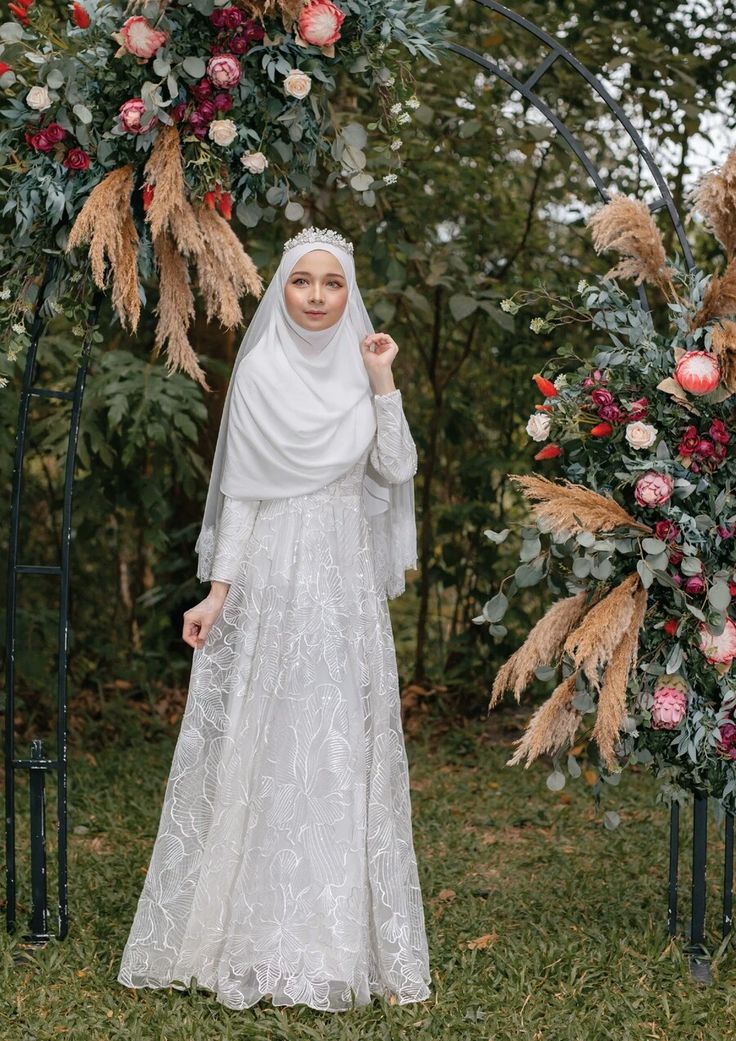 a woman in a white dress standing under a floral arch