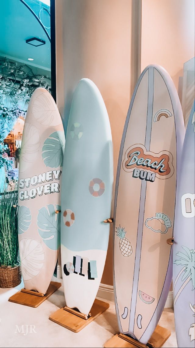 four surfboards are lined up on display in a room with plants and palm trees