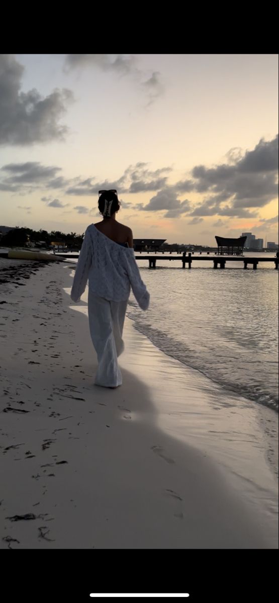 a woman walking on the beach at sunset